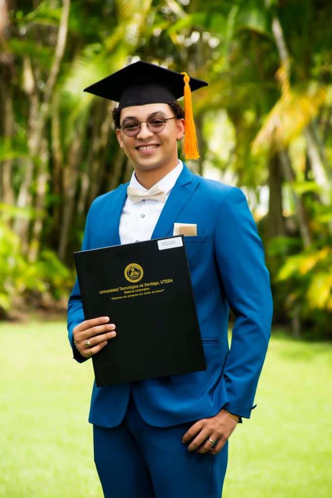 Young man in blue suit celebrating graduation outdoors with diploma.